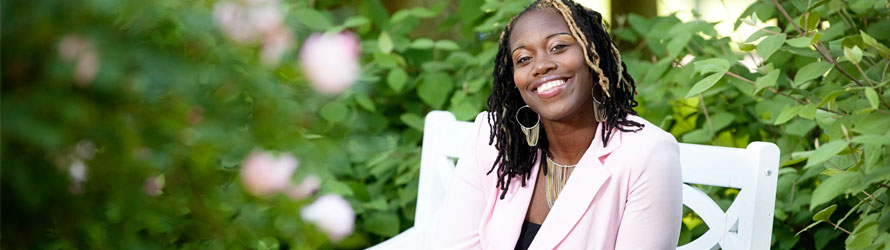 sul_31 woman smiling sitting on park bench with trees and flowers surrounding her, thinking about partnering with sullivan university for her company's employment needs