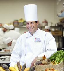 Chef Akmon 220x245 man in chefs uniform with a bunch of vegetables on the table